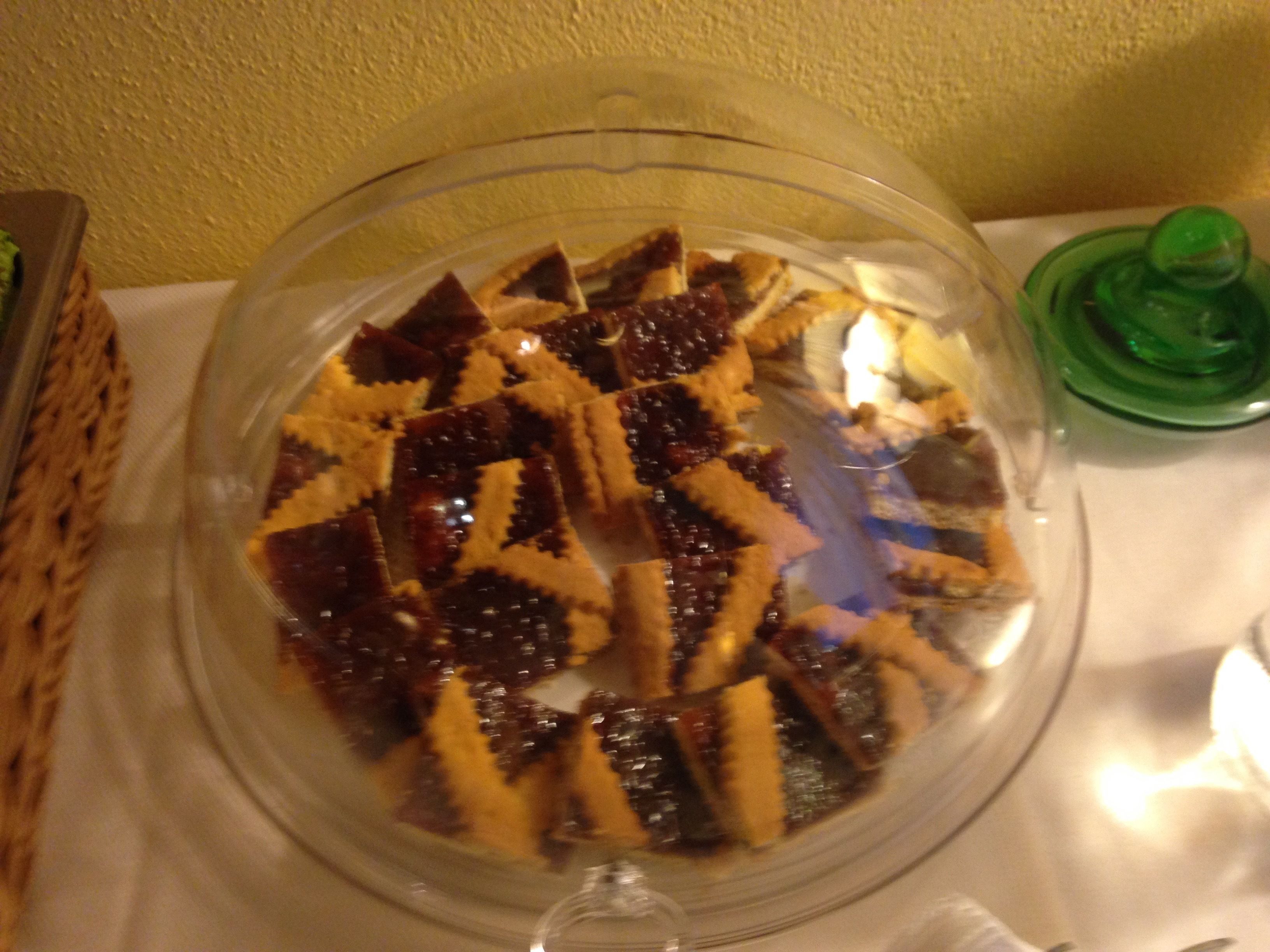 A dessert dish with a clear glass cover, a green lid, and a white tablecloth.