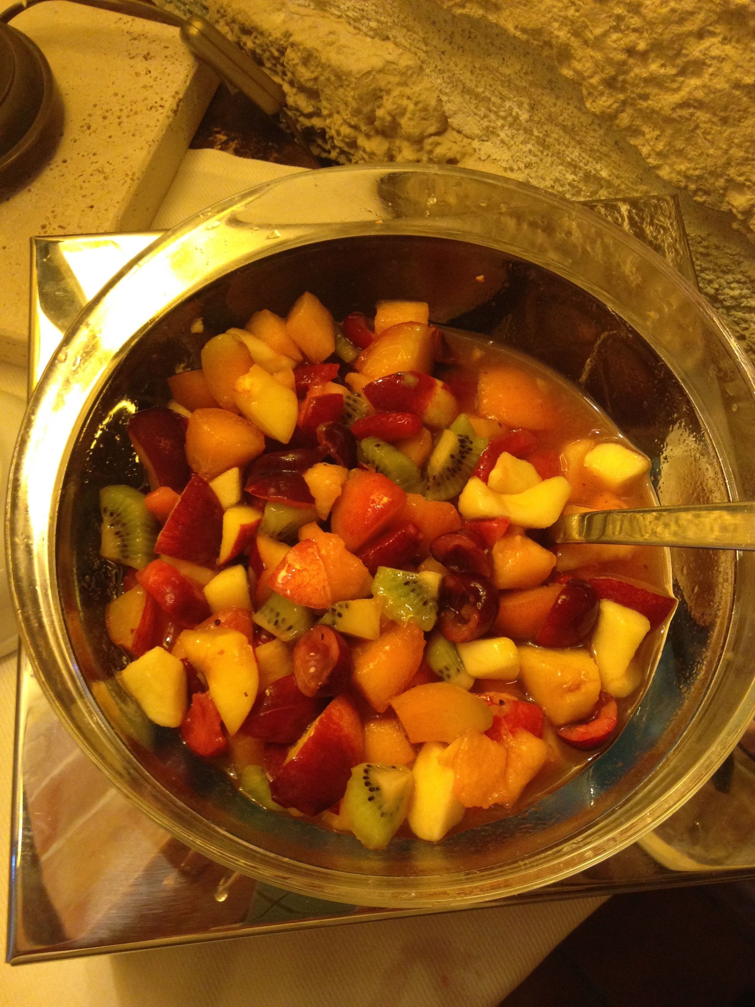 A bowl of mixed fruit salad with a spoon.
