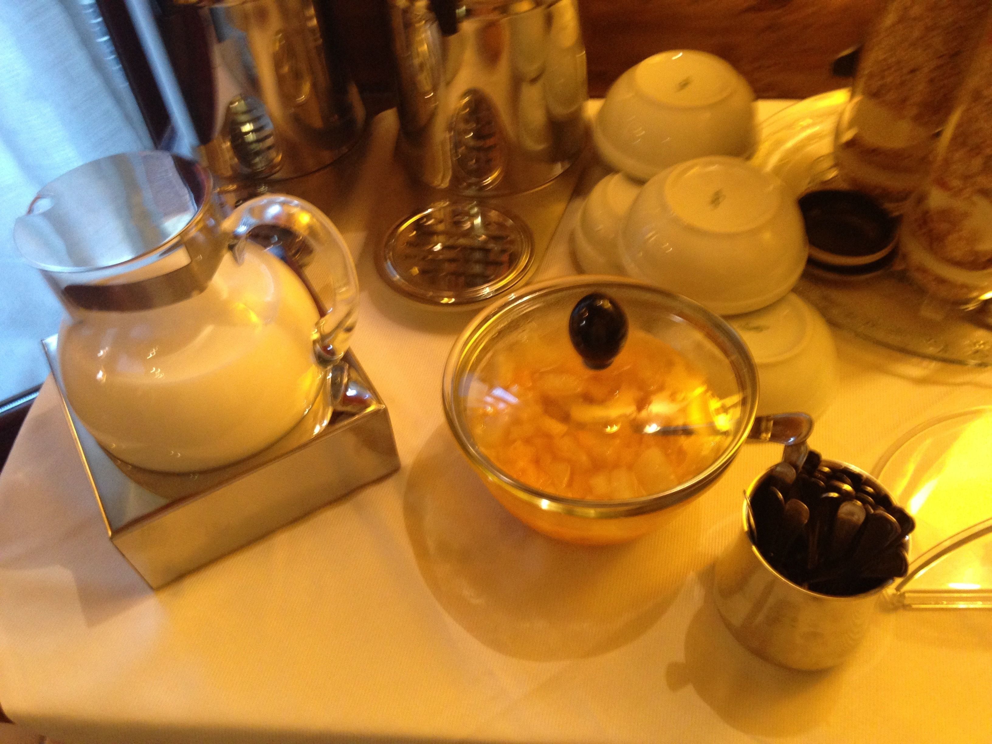 A table with a glass pitcher, a bowl with a lid, and a metal cup with coffee beans.