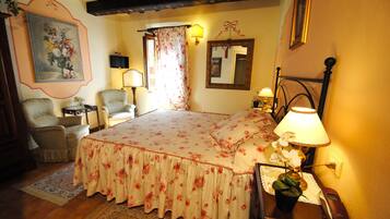 A bedroom with a floral bedspread, a bedside lamp, a chair, a small table, and a mirror on the wall.