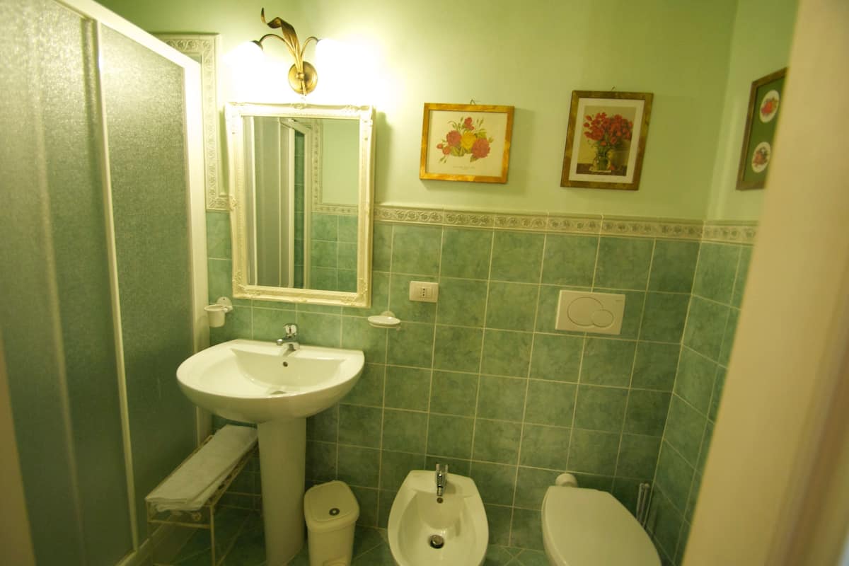 A bathroom with a pedestal sink, a urinal, and a toilet. There is a mirror above the sink and a framed picture on the wall.