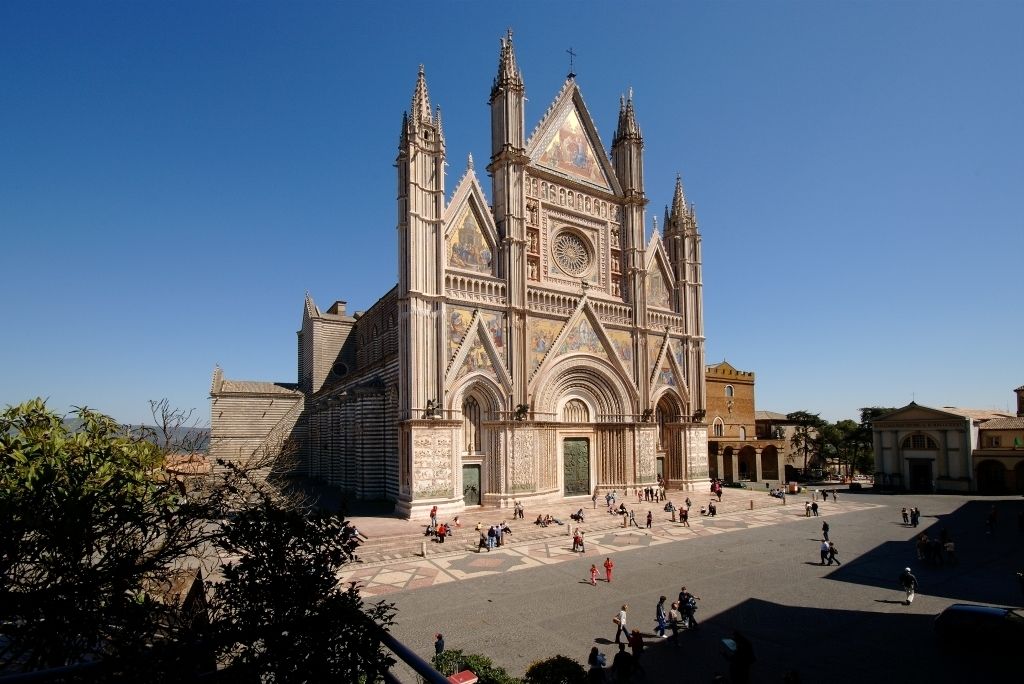 Una gran catedral con una cúpula central y varias torres, rodeada por una amplia plaza con gente caminando.
