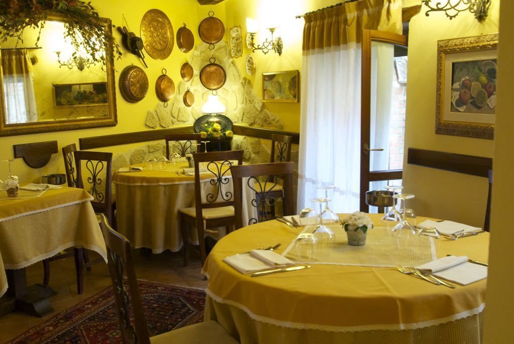 A dining area with round tables covered in yellow tablecloths, chairs, and a decorative wall with plates and a mirror.