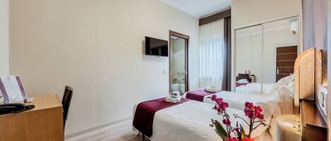 A hotel room with two beds, a desk with a telephone, a mirror, and a vase with flowers.