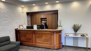 A reception area with a wooden reception desk, a grey sofa, and a small table with a vase and decorative items. - E H ROME AIRPORT (Fiumicino)