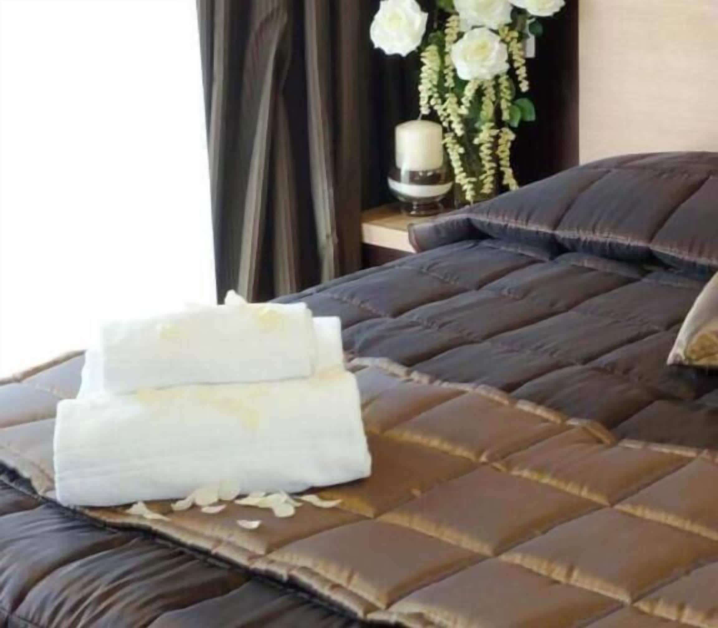 Un letto con copripiumino trapuntato marrone, un cuscino bianco e due asciugamani piegati con cura.