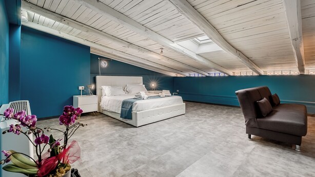 A bedroom with a bed, a chair, a nightstand, and a potted orchid. - E H ROME AIRPORT (Fiumicino)