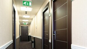A hotel hallway with dark patterned carpet, wooden doors, and a green exit sign. - E H ROME AIRPORT (Fiumicino)