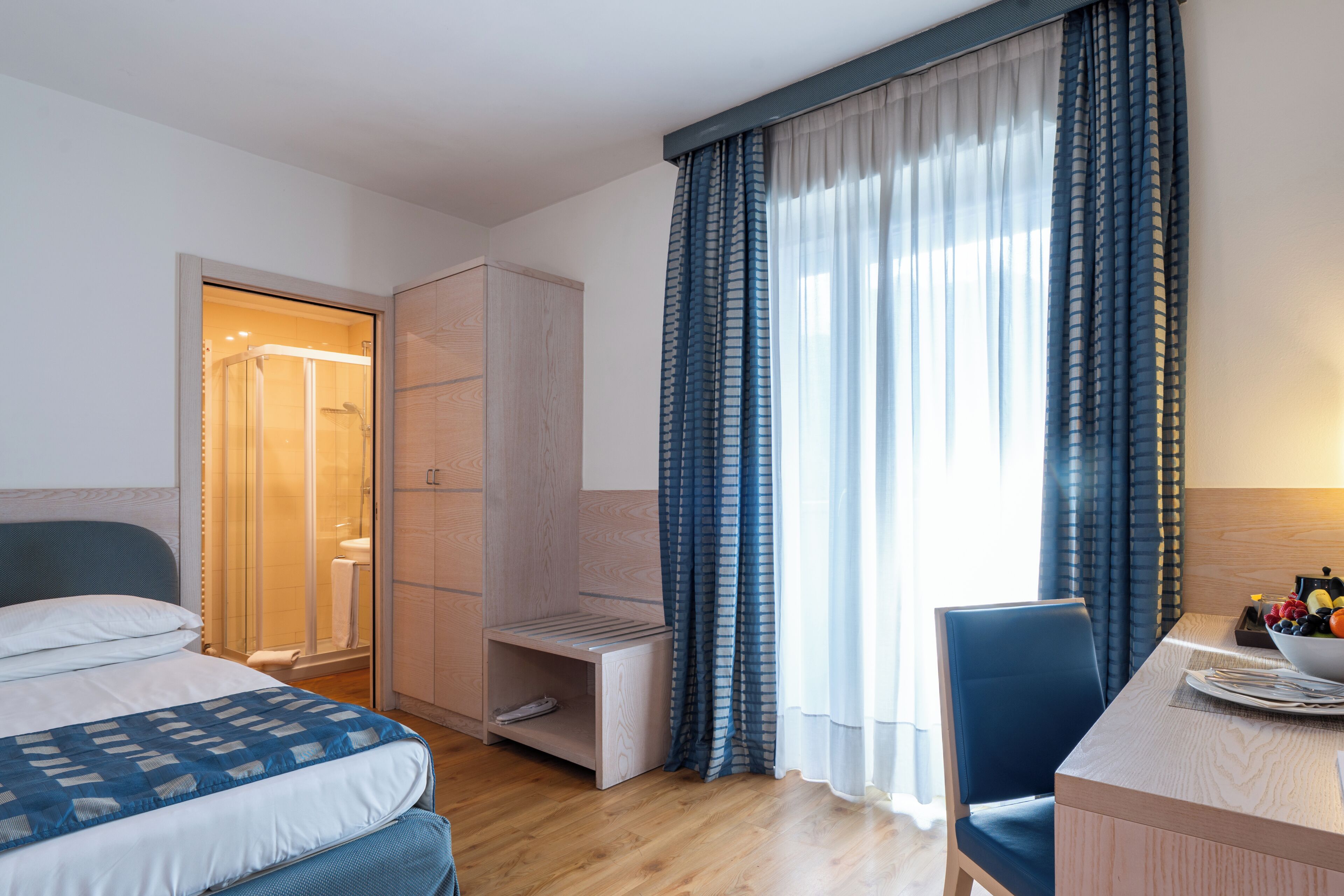 Habitación de hotel con cama, escritorio, silla, armario y zona de ducha.