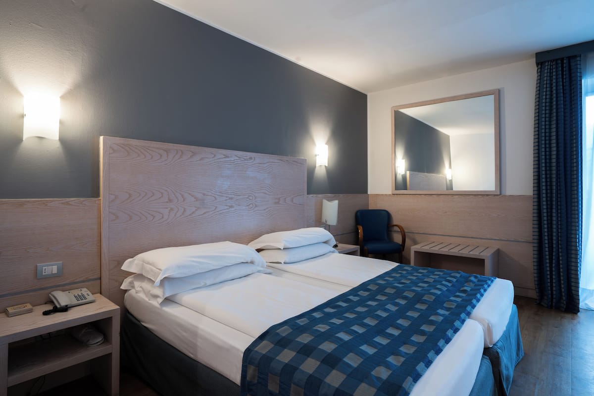 A hotel room with a large bed, bedside tables, a desk, a chair, a mirror, and a telephone.