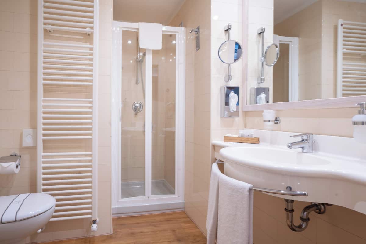 A bathroom with a glass-enclosed shower, a white sink, a mirror, and a toilet.