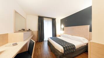 Ein Hotelzimmer mit Bett, Schreibtisch, Stuhl, Spiegel und einem Fenster mit Vorhängen.