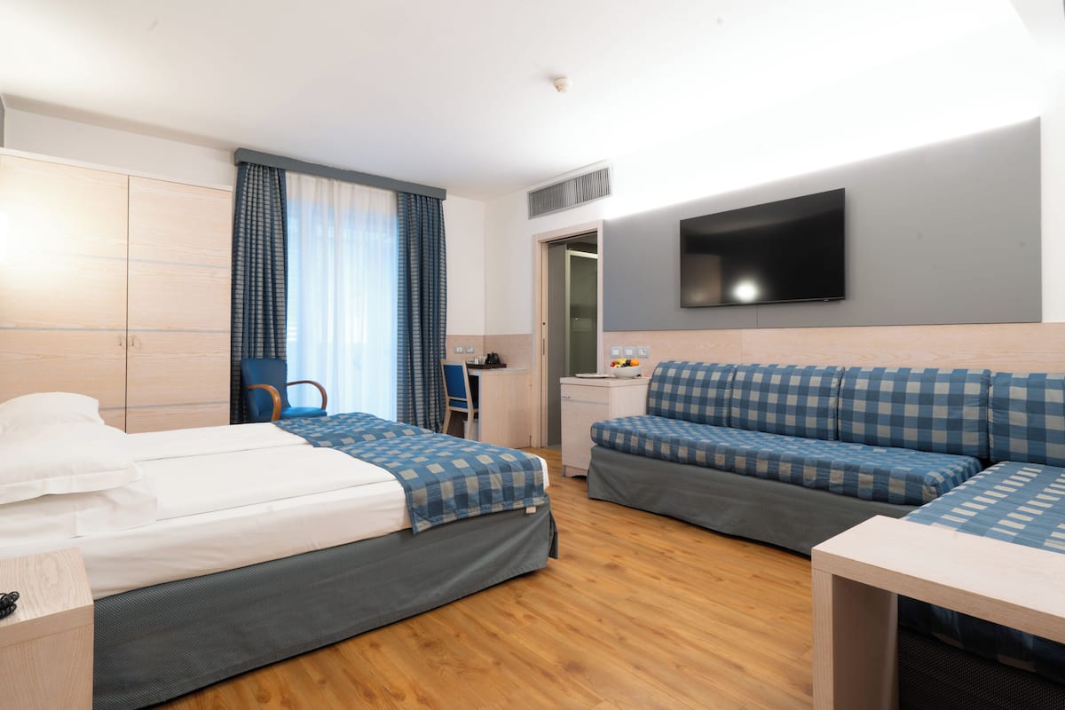 A hotel room with a bed, a desk, a chair, a sofa, and a TV.