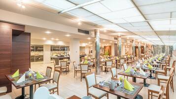 Ein geräumiges Restaurant mit mehreren Tischen und Stühlen, einer hohen Decke mit Oberlichtern und einem klaren, modernen Interieur.