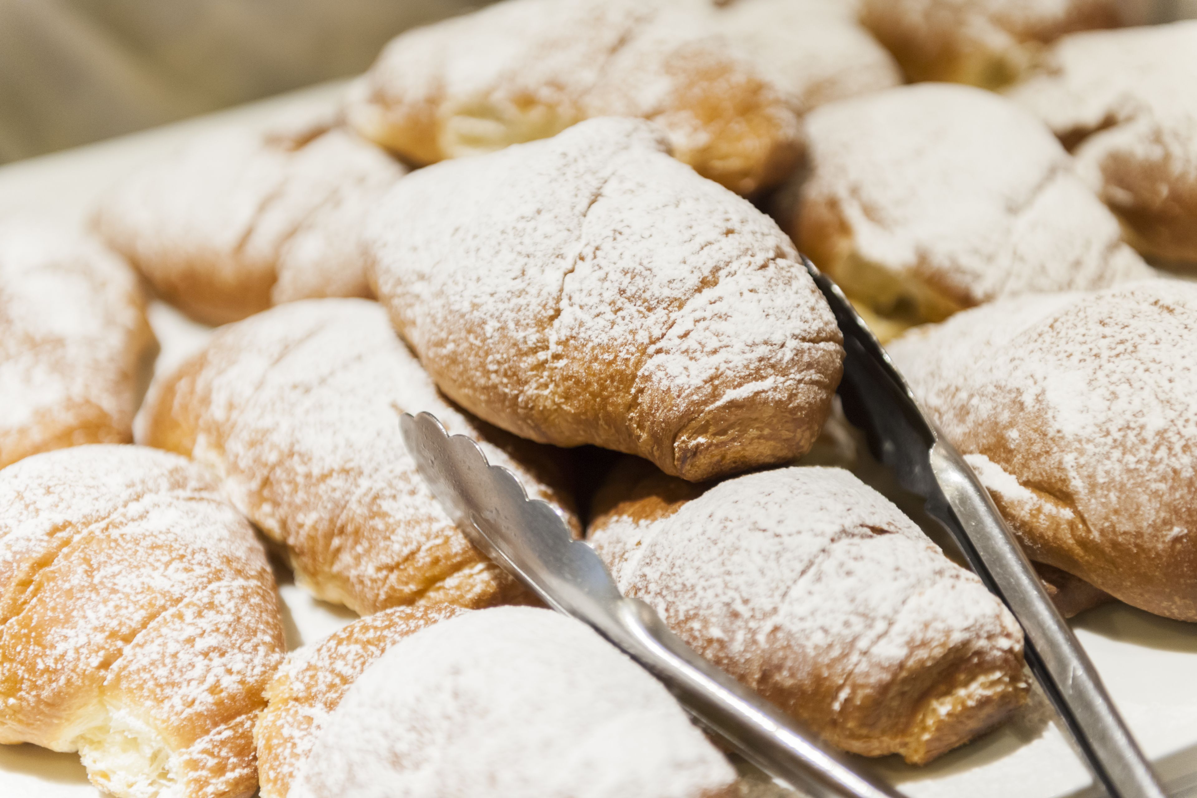 A tray of pastries dusted with powdered sugar, accompanied by a pair of tongs.