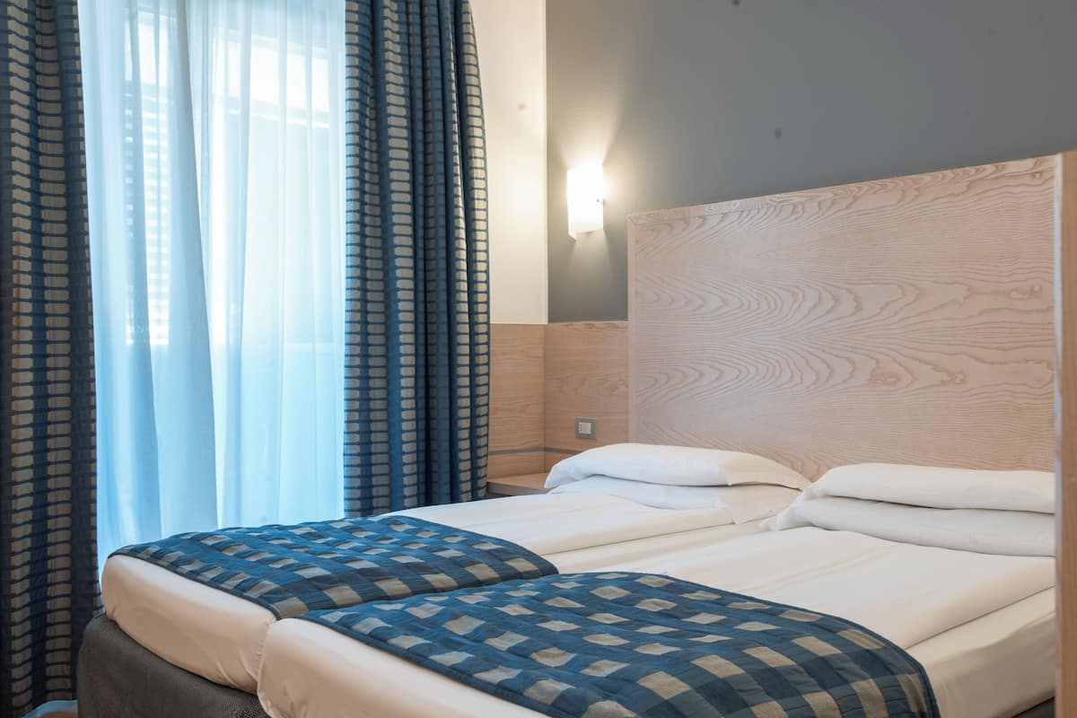 A hotel room with a bed, curtains, a wall-mounted light, and a wooden headboard.