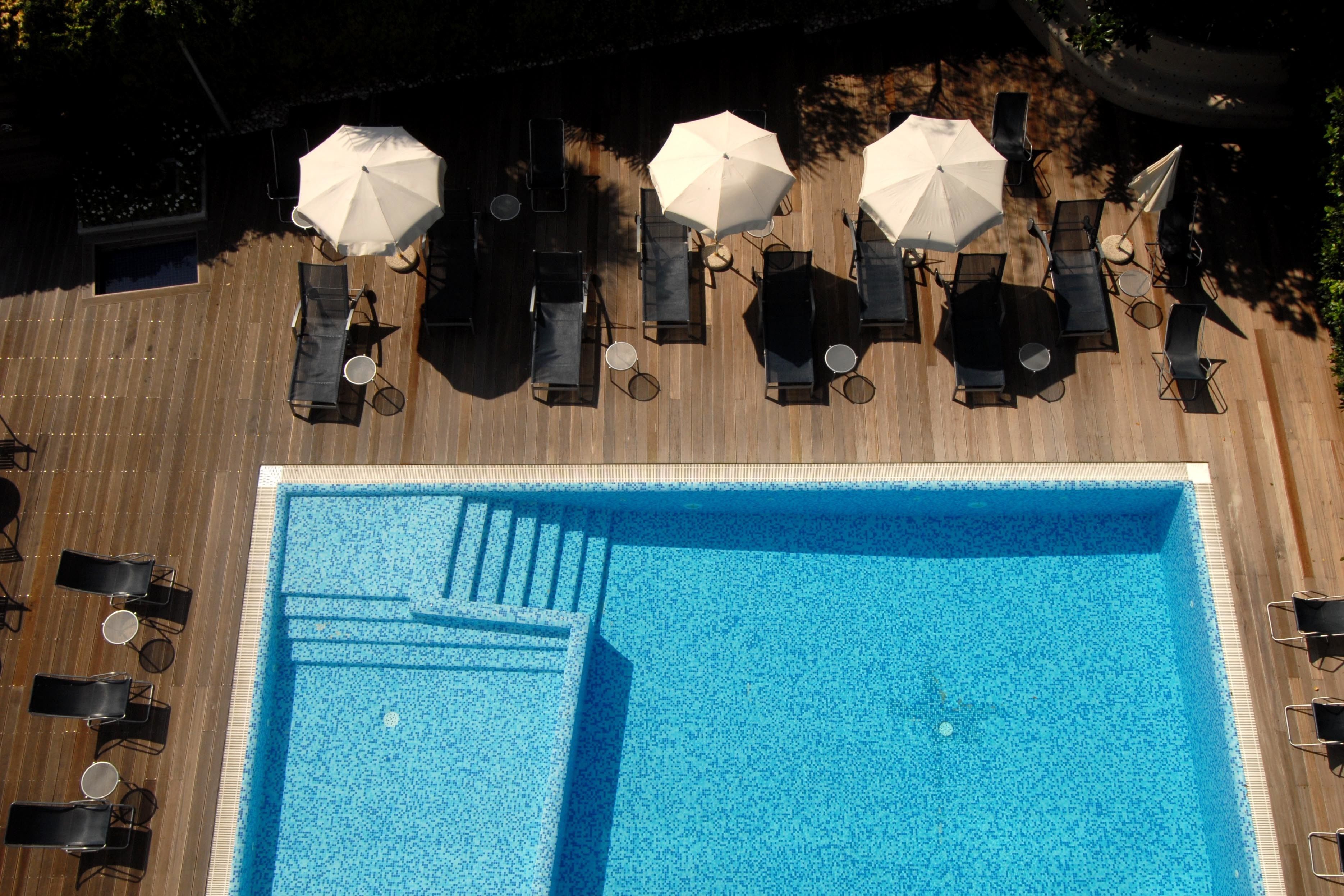 Un área de piscina en la azotea con sillones de descanso y sombrillas.
