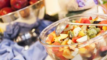 A bowl of fruit salad with a spoon, surrounded by other bowls and fruits.