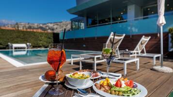 Une table à manger dressée avec un repas, des boissons, et une vue sur la piscine.
