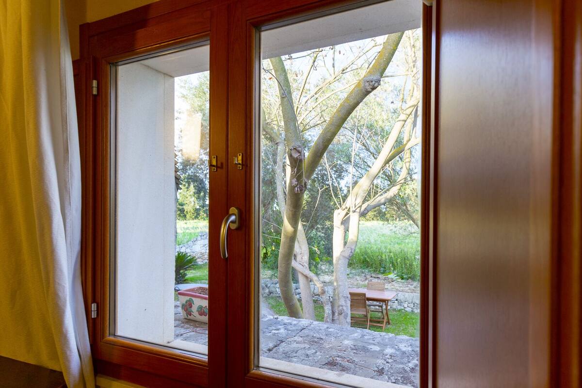 Puerta corrediza de vidrio que da a un patio exterior con una mesa y sillas de piedra, rodeado de árboles.