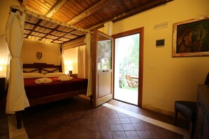 A bedroom with a wooden ceiling, a bed with a red bedspread, a white canopy, and a door leading to an outdoor area with a table and chairs. - Villa Dei Papiri (Syracuse)