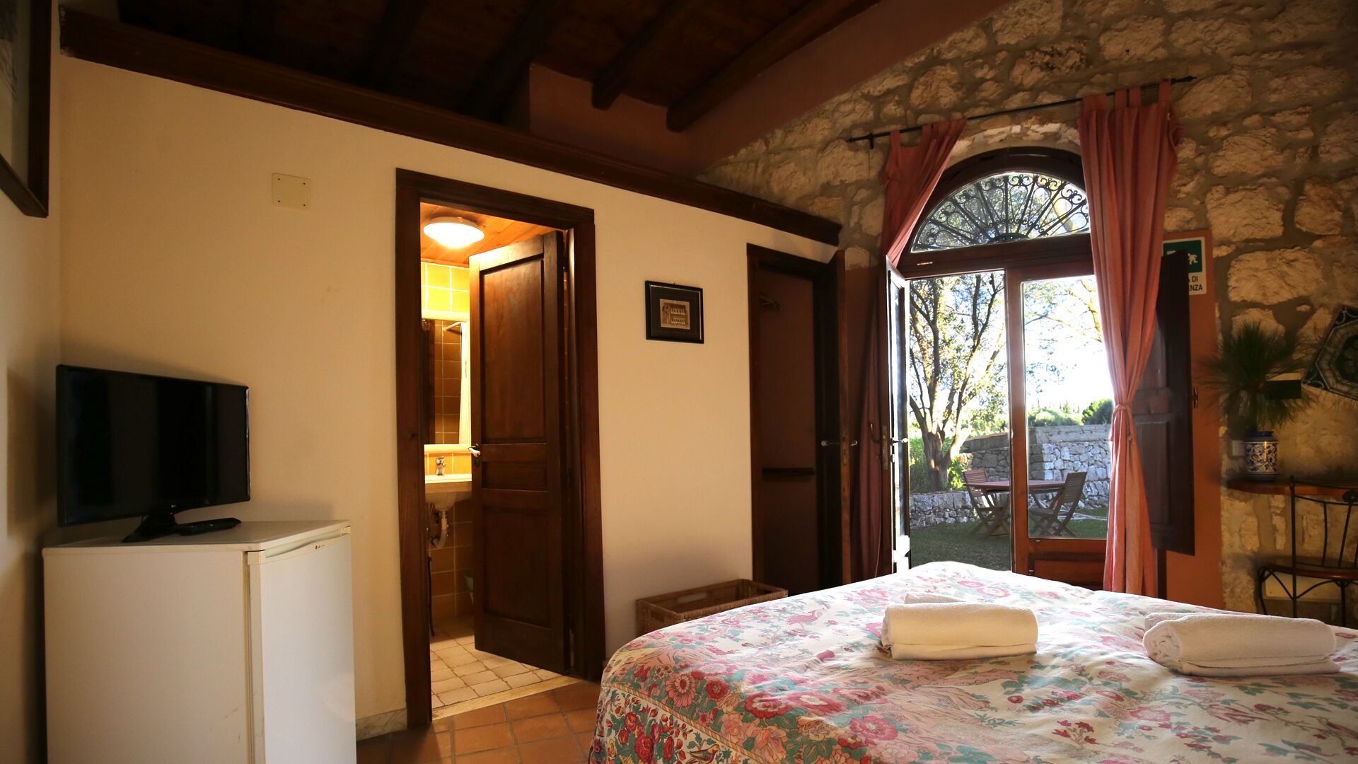 A bedroom with a bed, a television, a bathroom, and a view of the outdoors.