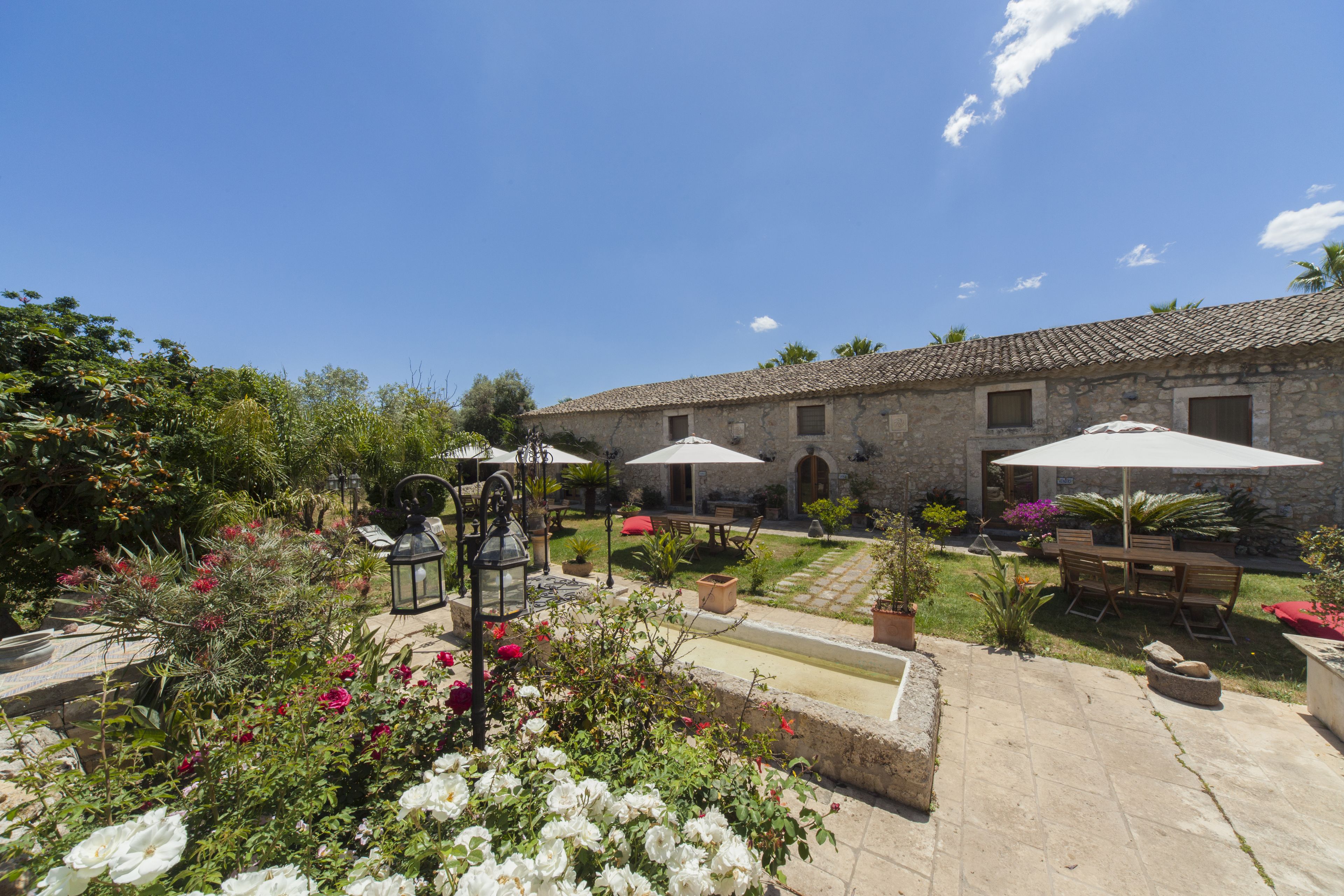A courtyard with stone buildings, outdoor furniture, and a variety of plants.