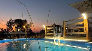 Una piscina con muelle de madera y escalera, rodeada de árboles y cielo al atardecer.