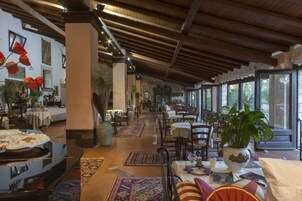Un restaurante espacioso con techos altos y vigas de madera, que cuenta con mesas dispuestas para comer y plantas en macetas.
