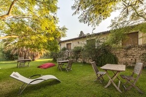 An outdoor patio with a table and chairs, a lounge chair, and a stone wall. - Villa Dei Papiri (Syracuse)