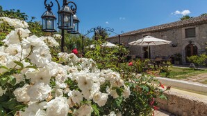 Un patio con rosales blancos, muros de piedra y mobiliario para exterior.