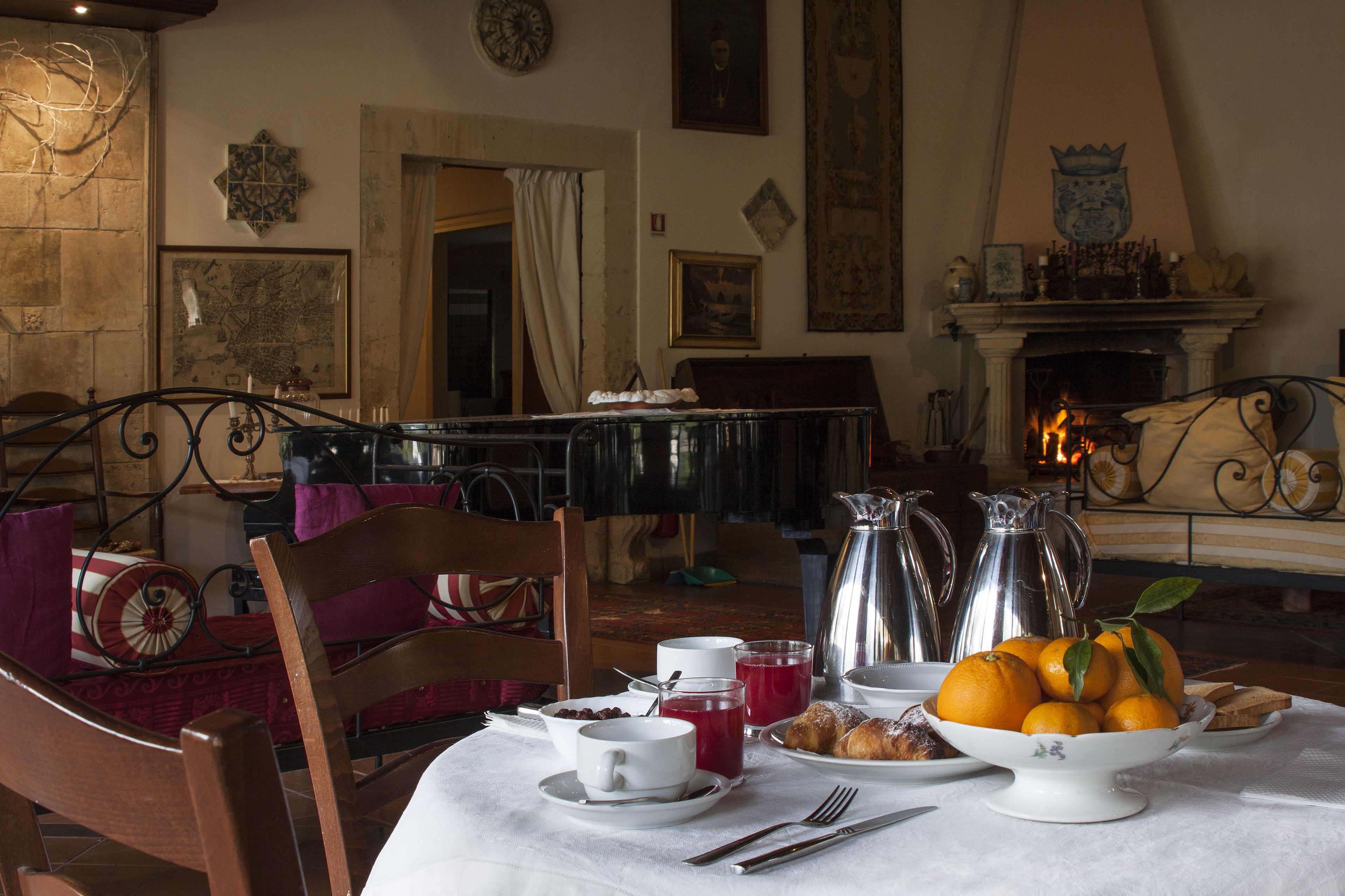 A dining area with a table set for breakfast, including a bowl of oranges, pastries, and a coffee pot.