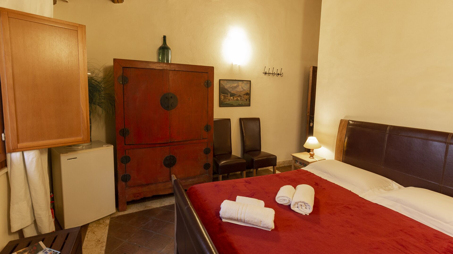 Una camera d'albergo con un letto, due poltrone, una scrivania, un armadio e una lampada.