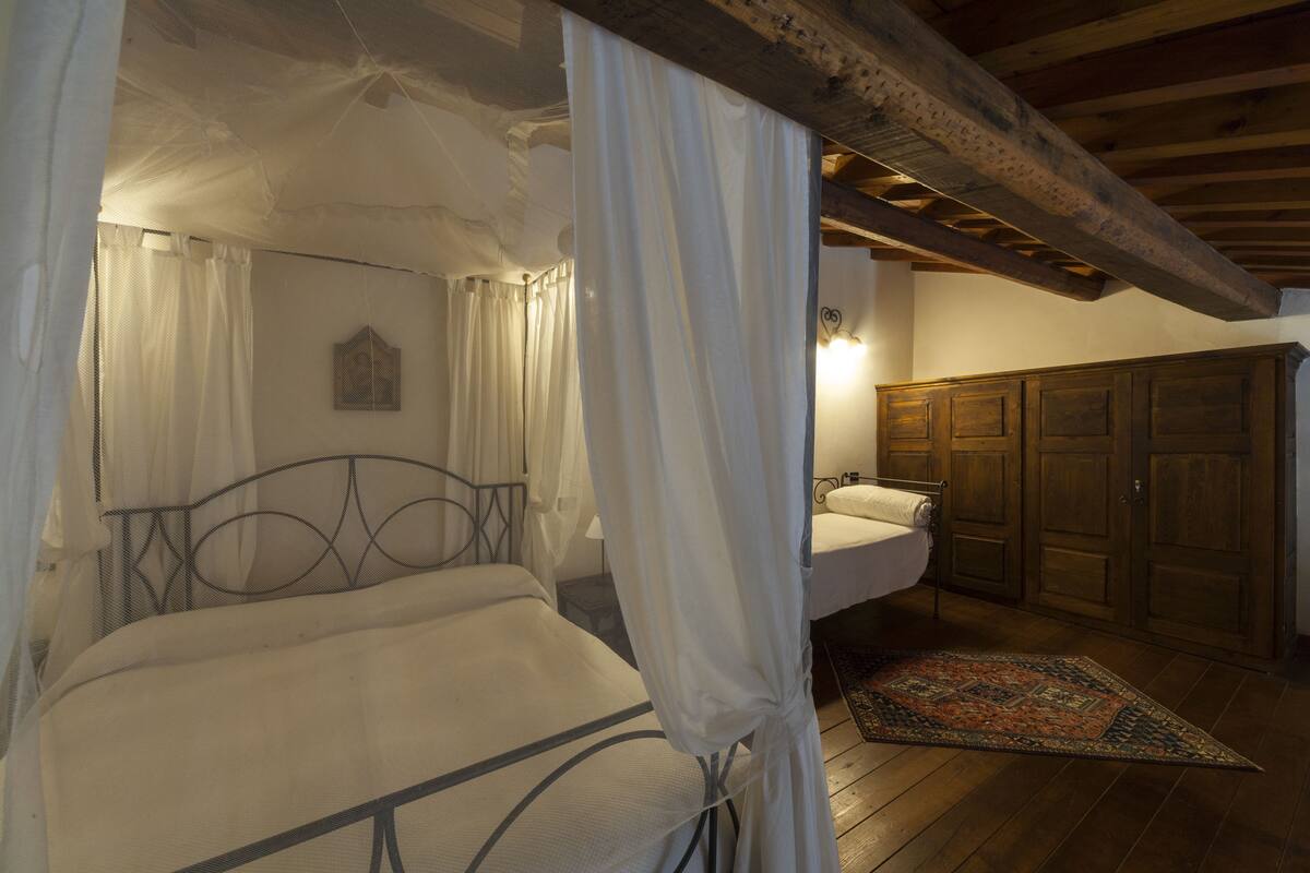 Un dormitorio con cama a dosel, mesita de noche, armario de madera y baño con lavamanos y espejo.