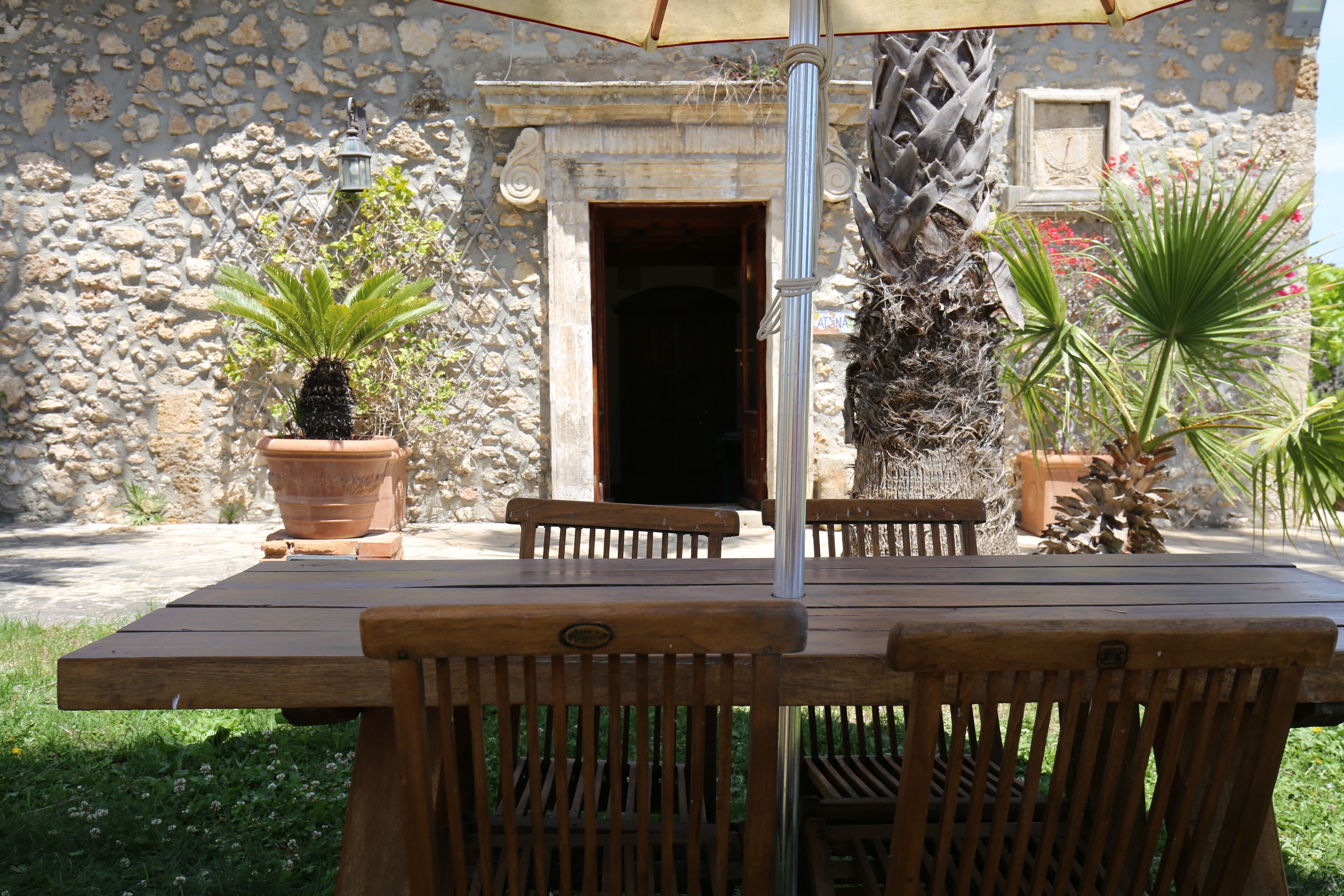Un espacio al aire libre con pared de piedra, plantas en macetas y mesa y sillas de madera.