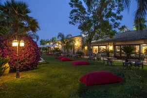 An outdoor seating area with tables and chairs, surrounded by lush greenery and flowering plants.