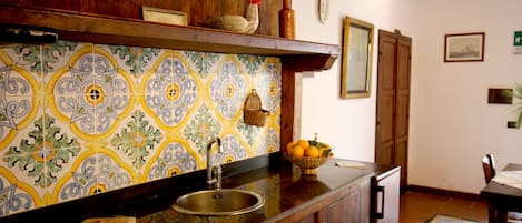 A kitchen with a tiled backsplash, wooden cabinets, a sink, and a fruit bowl on the counter.