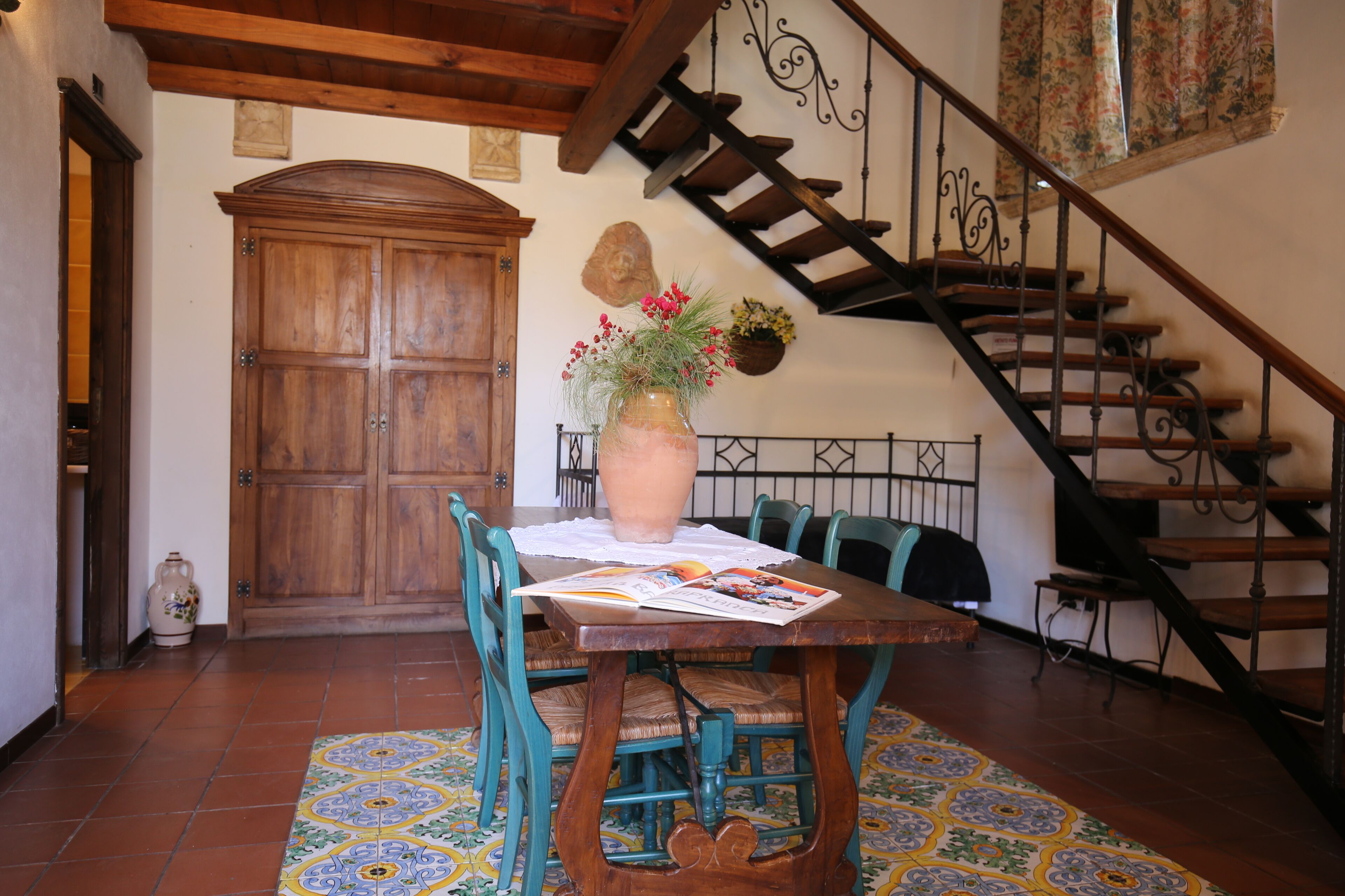 Ein Essbereich mit Holztisch, Stühlen, einer Blumenvase, einer Treppe und einer Holztür.