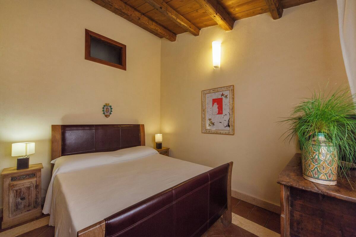 Un dormitorio con una cama de madera, lámparas de noche, un cuadro enmarco y una planta en maceta.