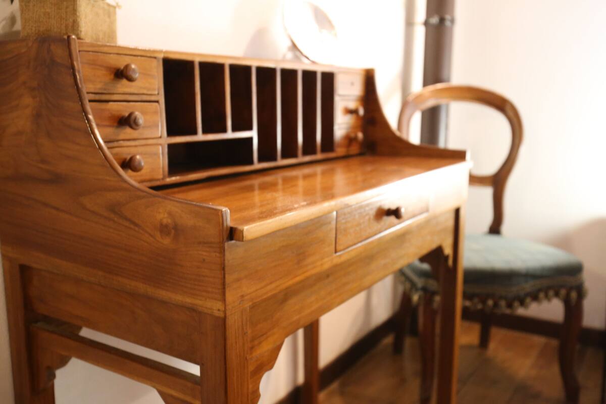 Un escritorio de madera con cajones y una estantería integrada, una silla y una lámpara en una habitación con suelo de baldosas.