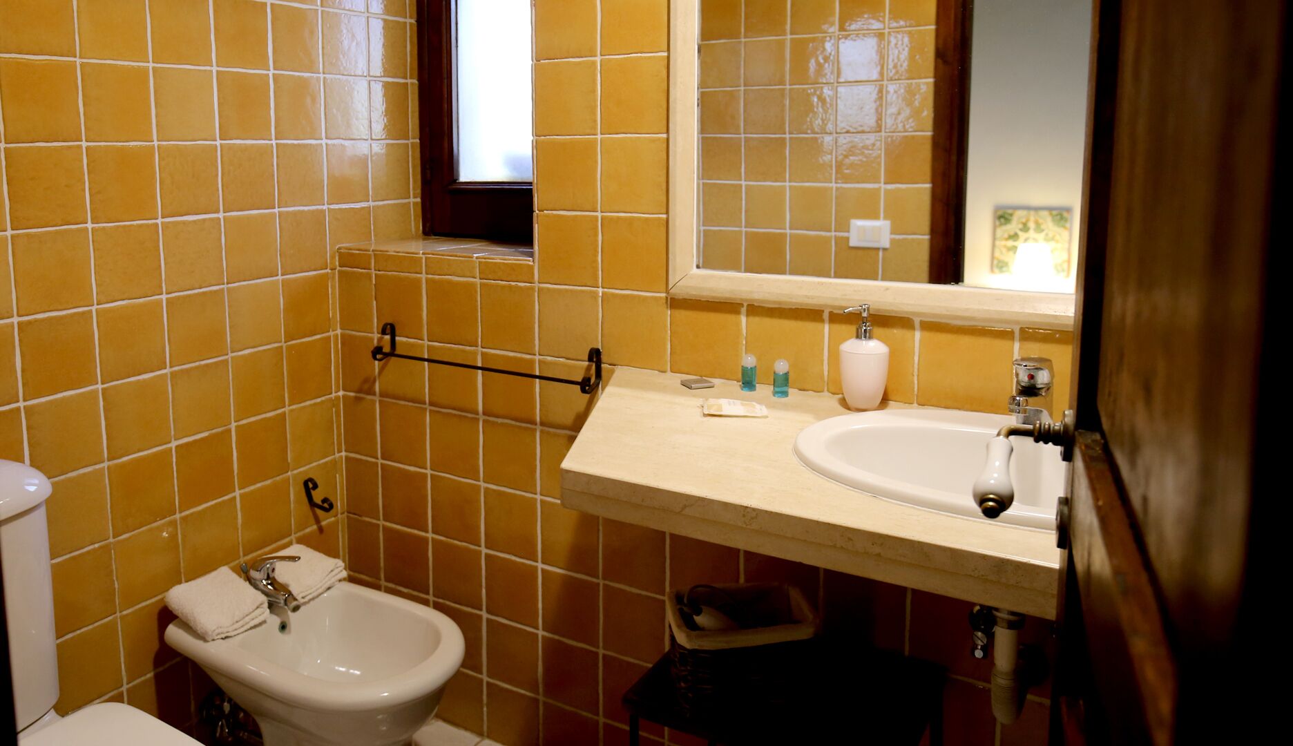 Ein Badezimmer mit gelben Fliesen, einem weißen Waschbecken, einem Bidet und einem Spiegel über dem Waschbecken.