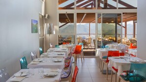 Un restaurante con varias mesas dispuestas para comer, grandes ventanales que ofrecen vistas a la montaña y un techo alto con vigas de madera.