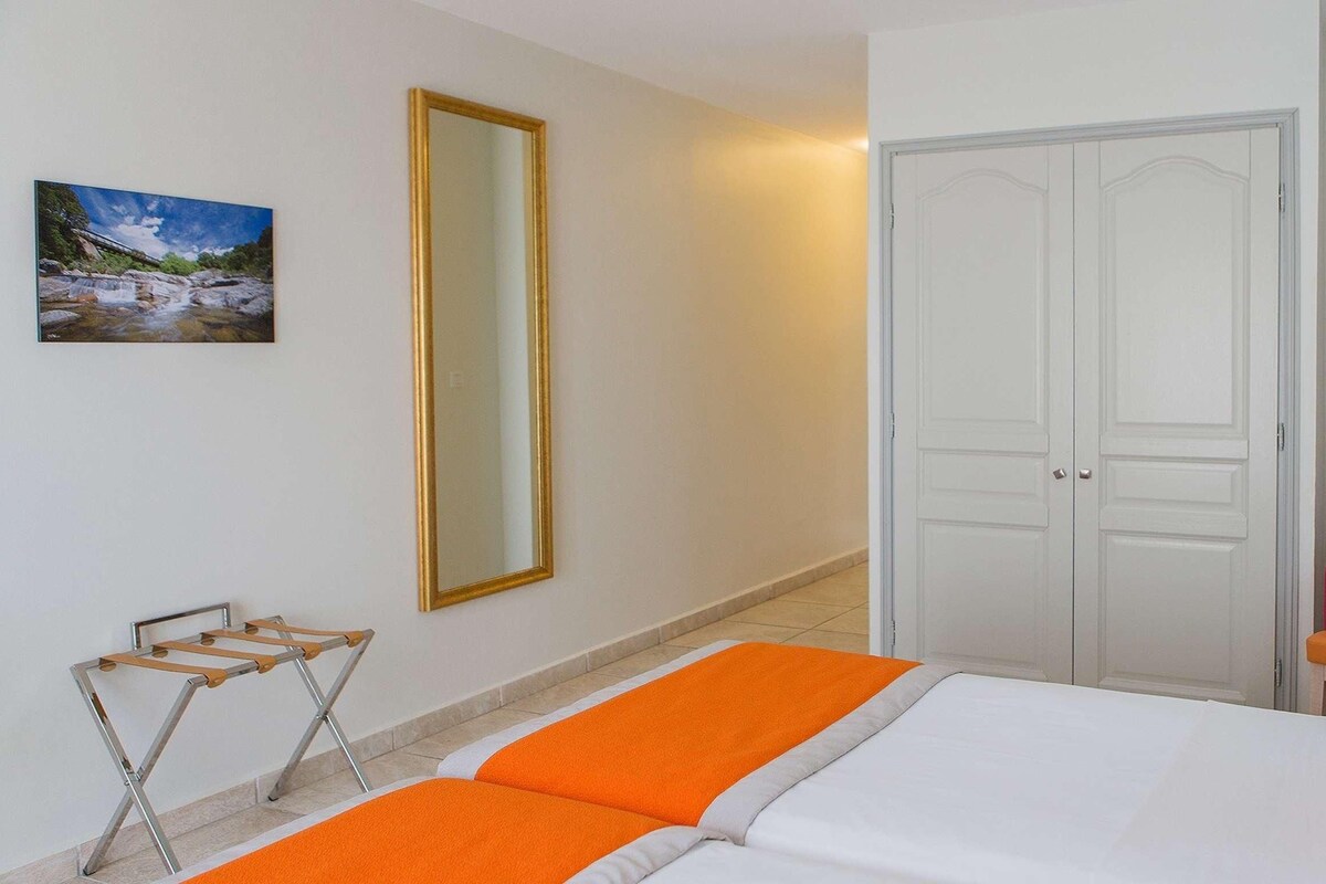 A hotel room with a bed, a chair, a wardrobe, and a mirror.