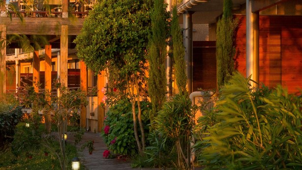 Un hotel con un jardín exuberante, un sendero de madera y un balcón con mobiliario exterior.