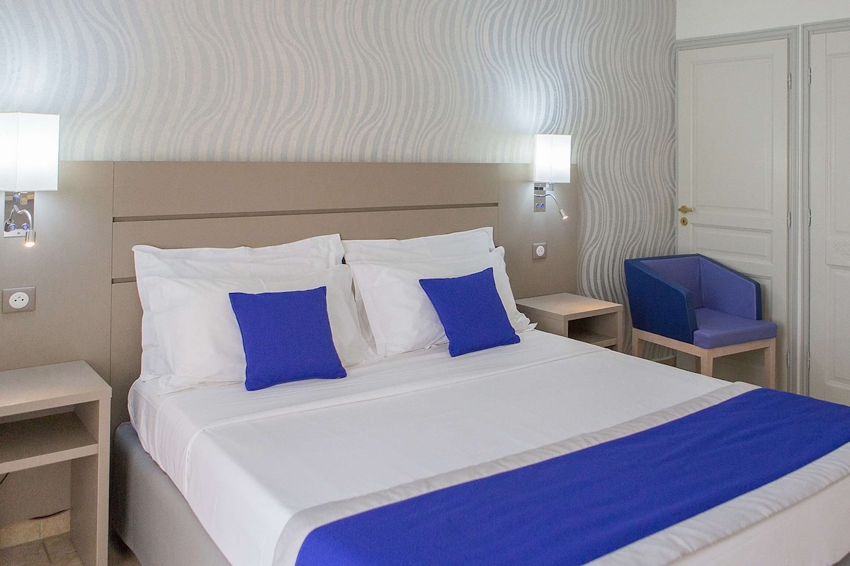 A hotel room with a bed, two nightstands, a chair, and a wardrobe.