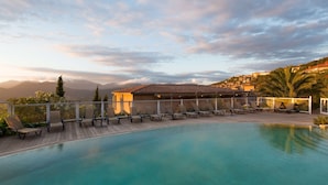 Zona de piscina con sillones de descanso y un edificio al fondo.