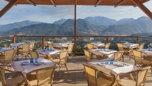 Un área de comedor al aire libre con mesas y sillas, con vistas a un paisaje montañoso.