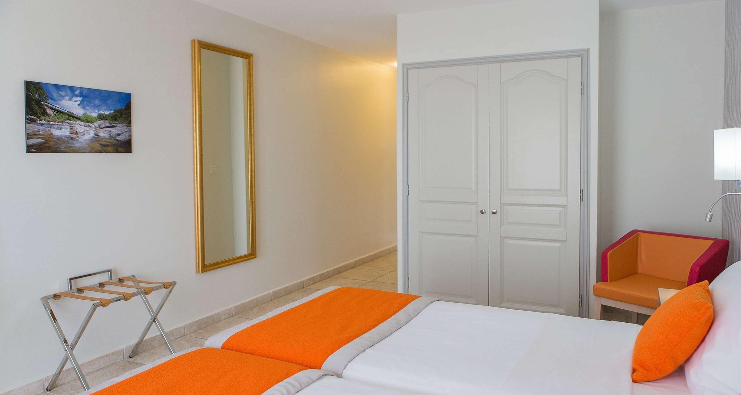 Une chambre d’hôtel avec un lit, une armoire, une chaise, un miroir et un tableau au mur.