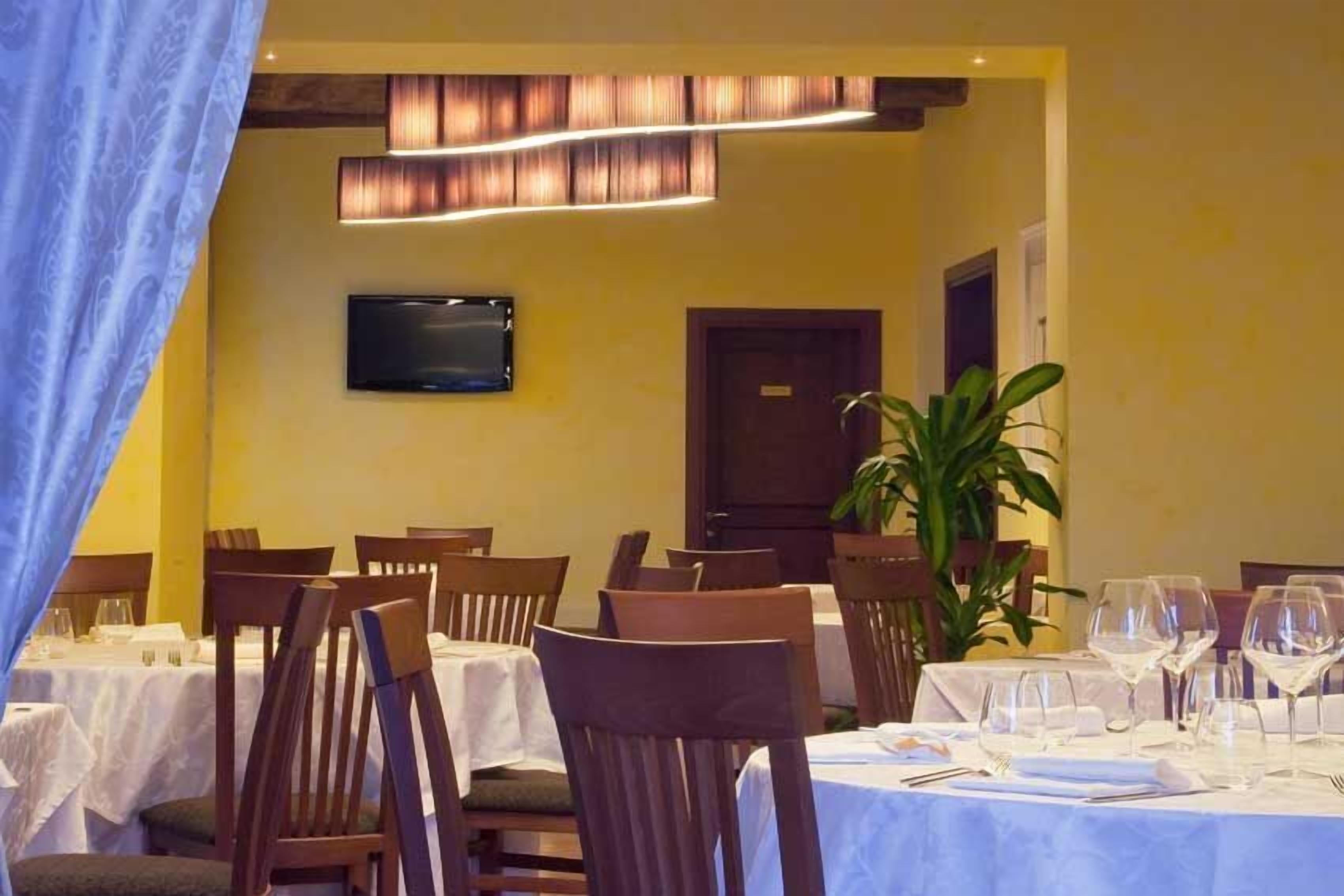 A dining area with tables set for a meal, chairs, a television on the wall, and a door in the background.