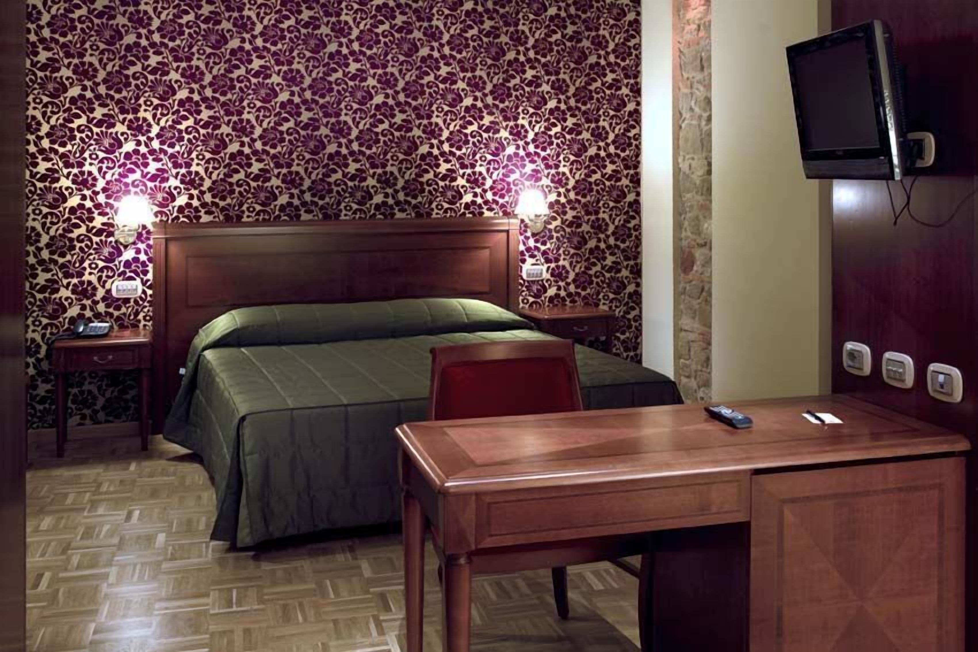 Ein Hotelzimmer mit einem Bett, einem Schreibtisch, einem Stuhl, einem Fernseher und zwei Nachttischlampen.